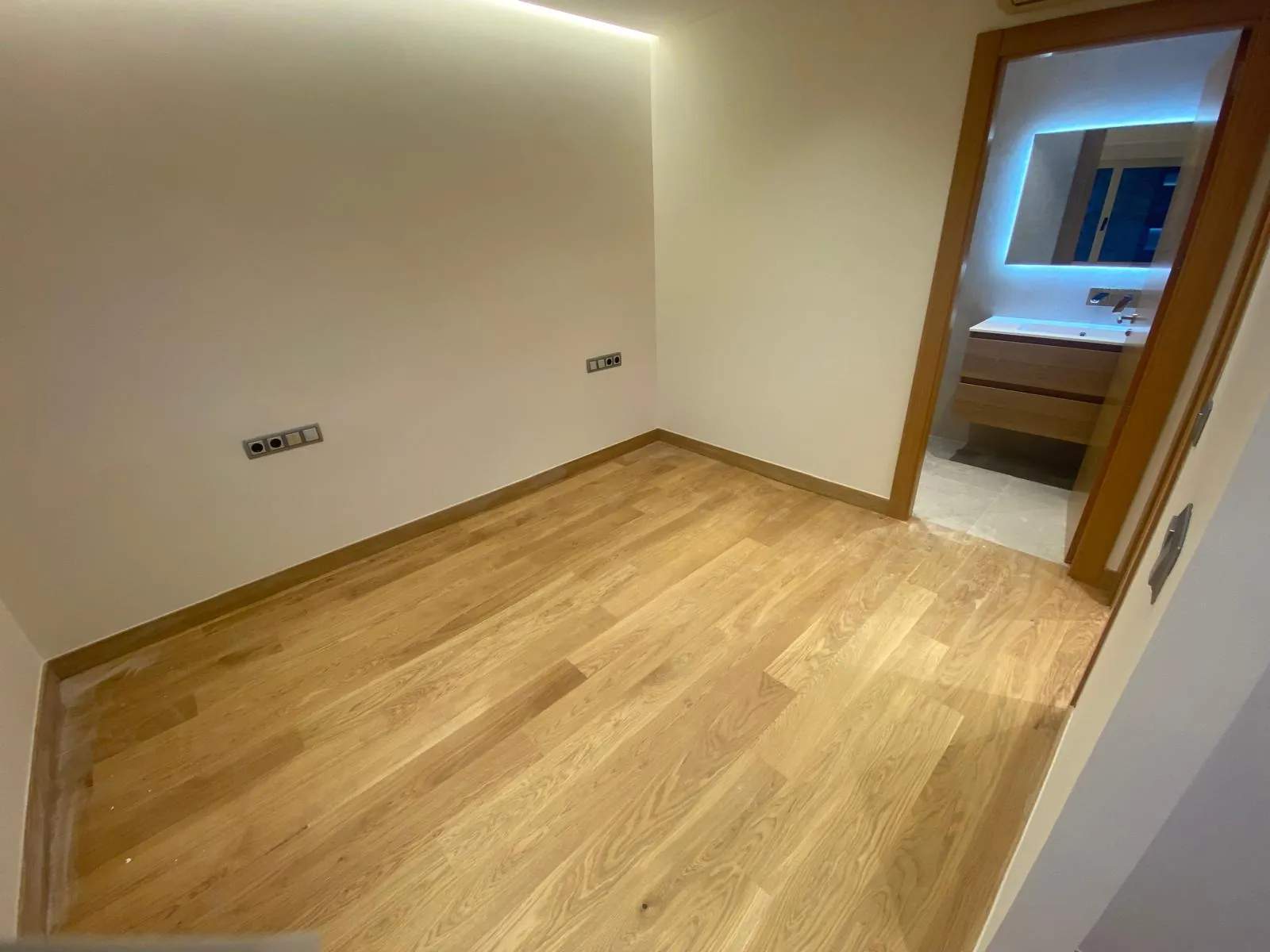 Estancia con suelo de madera natural, tira LED en el techo y baño en suite