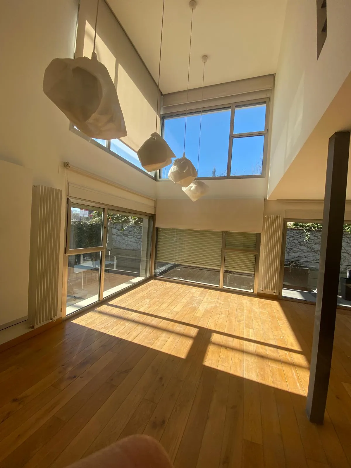 Salón a doble altura con suelo de madera y grandes ventanales
