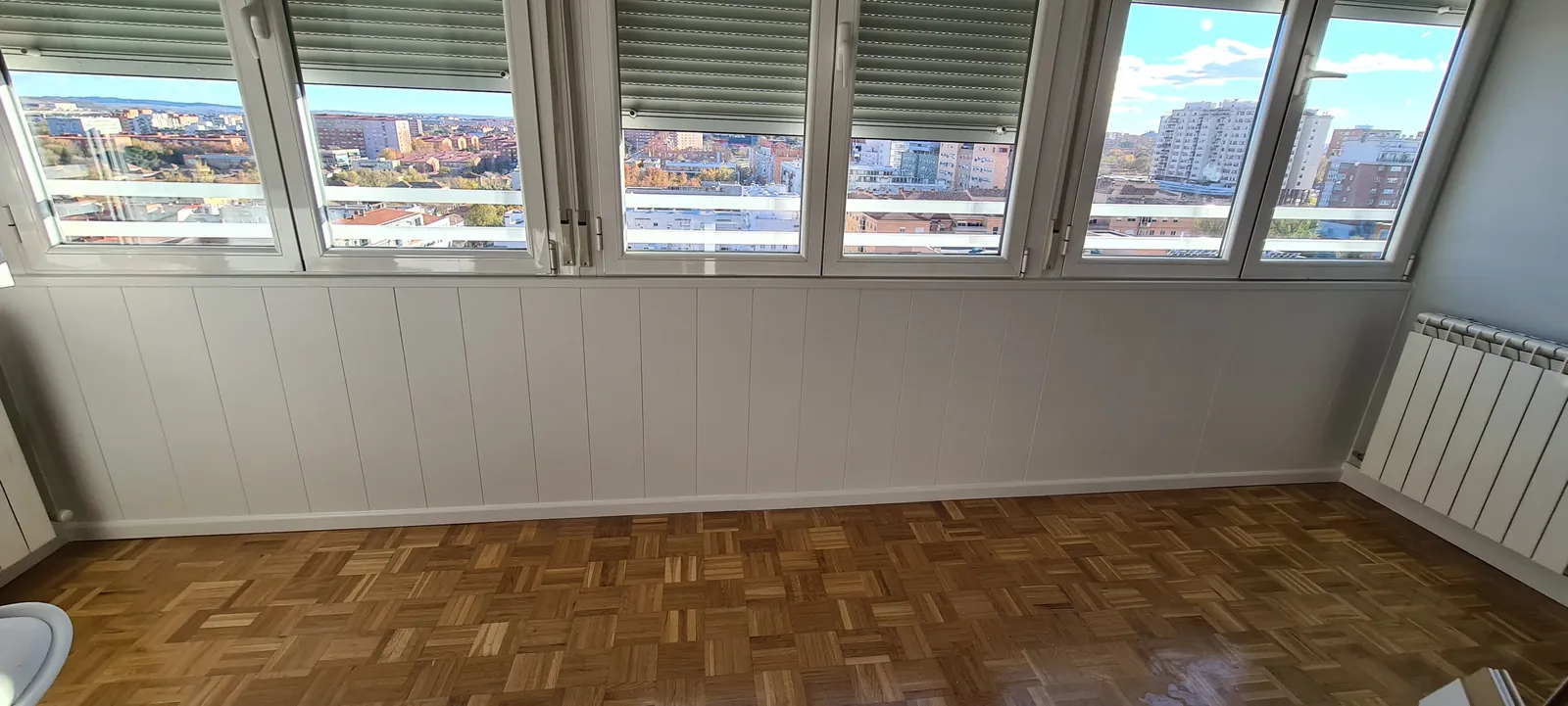 Salón con friso de paneles blancos bajo el ventanal y paredes en gris claro