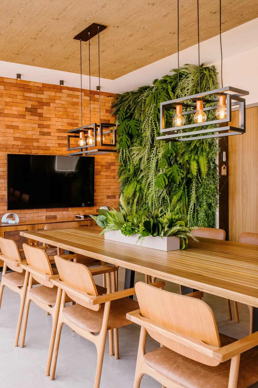 Oficina con mesa de reuniones de madera, pared de ladrillo y jardín vertical